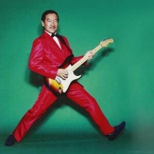Masayoshi Takanaka wearing a red suit and playing guitar
