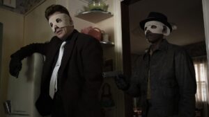 Two thieves wear masks and stand in a kitchen