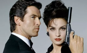 Two dark-haired figures in black clothes stare in different directions. One holds a silenced pistol
