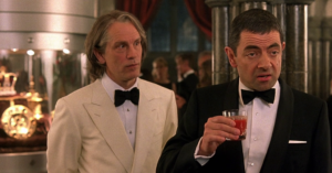 A spy holds a cocktail while a man in a bowtail and white suit looks at him in confusion