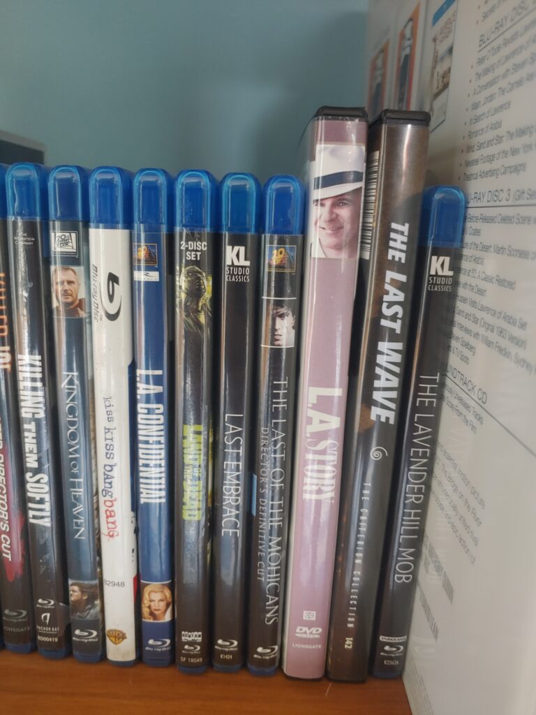 A series of blu ray cases on a bookshelf, sorted alphabetically