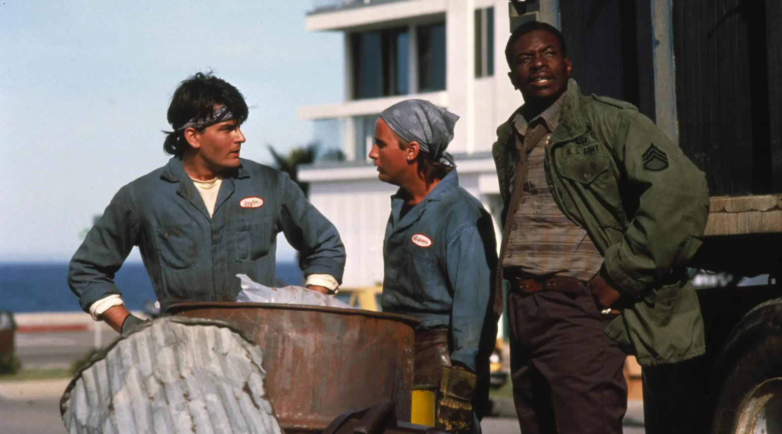 Two trash collectors argue next to a garbage can while a supervisor stands nearby and looks worried