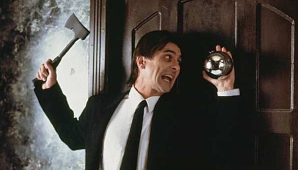 A man in a black suit holds a hatchet in one hand while his other hand is pinned to a door by a flying metal sphere