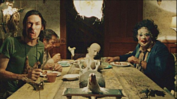 Four members of a cannibalistic family sit around a dinner table and look directly toward the viewer.