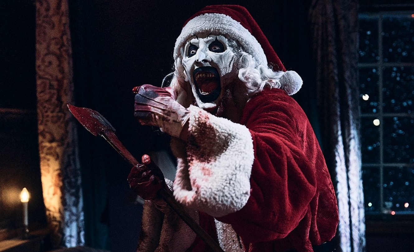 A killer clown is dressed in a Santa costume and holds an axe.